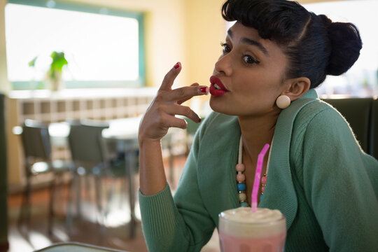Milkshake with whipped cream and pink straw sitting on table near bright window and plant