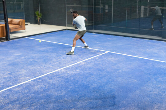 Man preparing backhand return on sports court, incoming yellow ball causing animated arc over glass