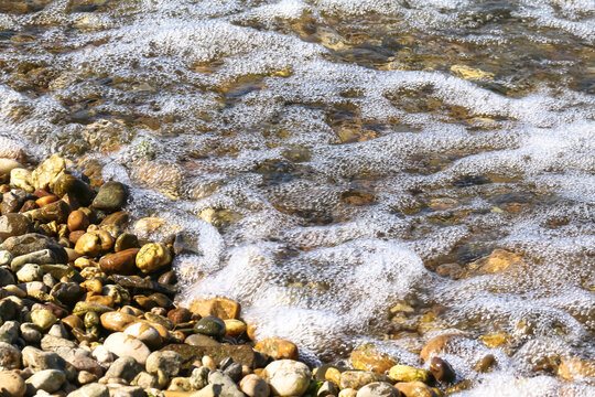 Sch&auml;umendes Wasser, Wellen treffen auf Kieselsteine