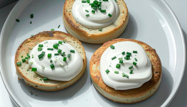 Toasted bread rounds topped with cream cheese and fresh chives on a white plate