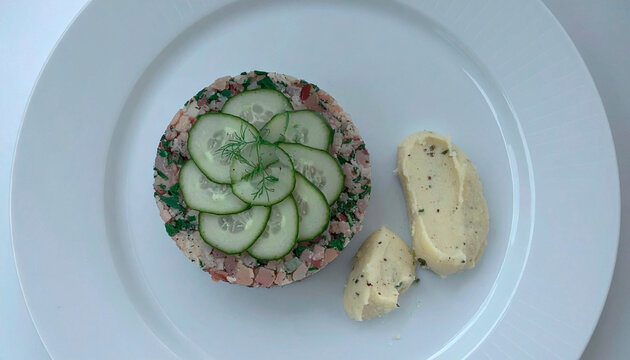 Meat tartare topped with fresh cucumber slices served with herb mashed potatoes on white plate