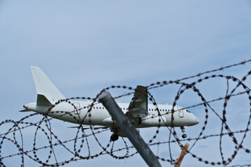 Jet Landing: White Plane, Barbed Wire and Cloudy Sky. White Passenger Plane Landing at Airport over Barbed Wire Fence under Cloudy Sky © Maksim Mikhailov