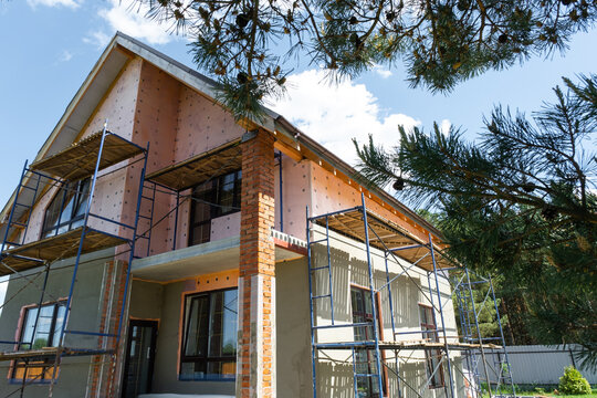 Construction with external render, facade insulation stage, wall plaster, surface smoothing, scaffolded finishing, preparation, protection, renovation works.