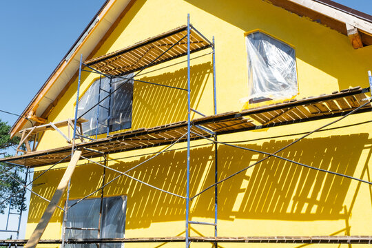 Facade painting on plaster, exterior finish, timber boards for decorative half-timber effect, scaffolding setup, house improvement and final renovation stage.