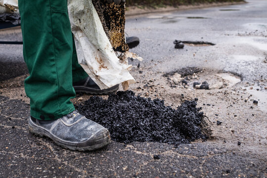 Road workers repair a pothole on a street by pouring asphalt from a bag.