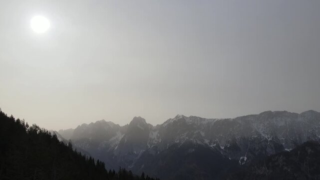 Aerial drone footage panning across dramatic mountain range and alpine foothills under hazy sky