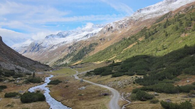 Aerial drone footage of alpine valley with mountain stream winding path and rugged peaks in Zillertal Austrian Alps