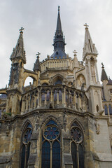 Obraz premium Gothic spires rise above ornate arches and statues against a bright sky. Stone tracery and stained glass frame the cathedral in Reims. Light and shadows reveal details across the facade.