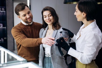 Naklejka premium Young couple selecting luxury jewelry, receiving assistance from a professional sales consultant in a modern boutique store