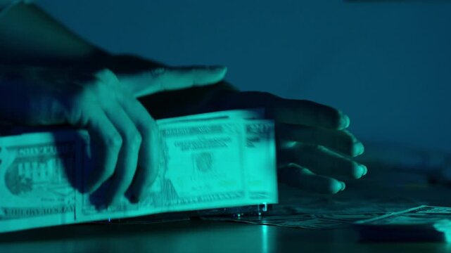 A woman organizes scattered US dollar bills into an even stack under soft blue lighting, her hands carefully arranging the notes on the table
