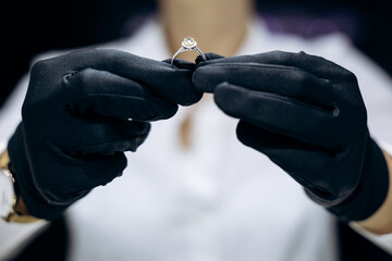Professional jeweler's gloved hands carefully examining a diamond engagement ring, ensuring quality...