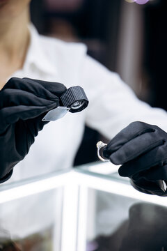 Gloved hands of a jewelry expert inspecting and appraising a diamond ring with a loupe over a white display case