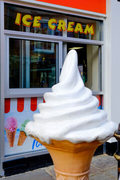 Large soft serve ice cream cone outside shop, colorful street scene