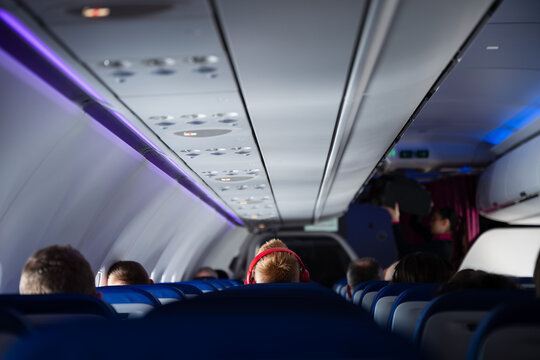 Interior view of a modern airplane cabin with passenger with red headphones seated and blue ambient lighting during a commercial flight