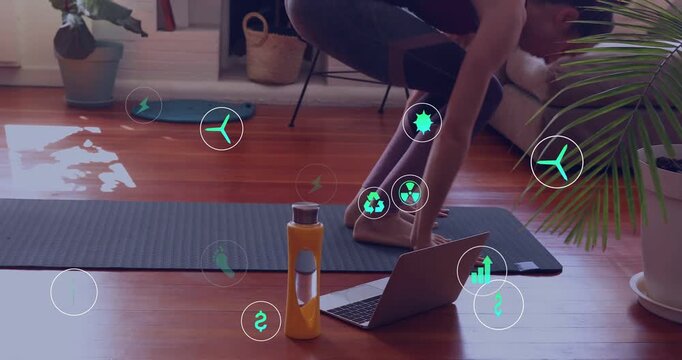 Woman following laptop cue, doing burpees on mat for fitness, green icons floating around her