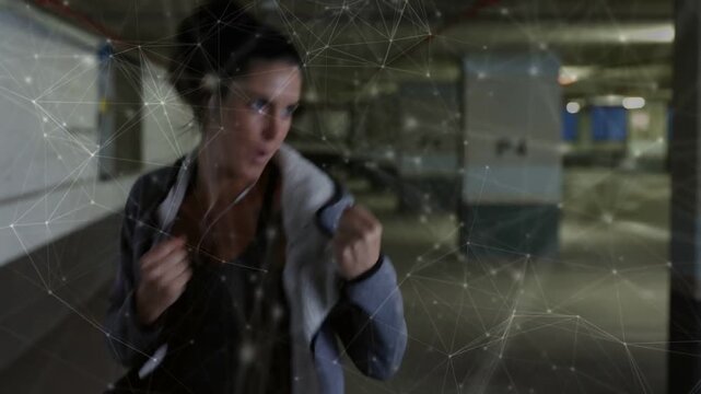 Woman rising from crouch with hoodie and training shadowboxing in garage, overlay crossing subject