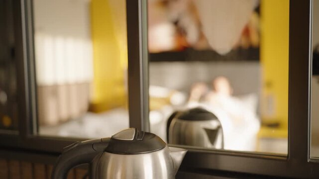 A kettle boiling near a mirror creates steam and condensation, with a reflection of a warm, bright bedroom featuring soft tones and yellow accents in a serene morning setting