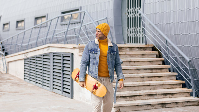 Man with skateboard walking on street with urban tattoos