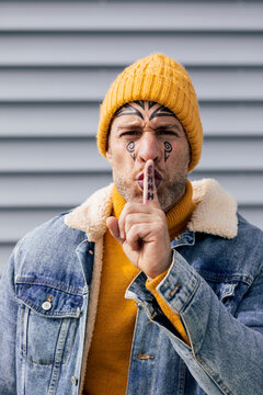 Man with facial tattoos signaling silence outdoors