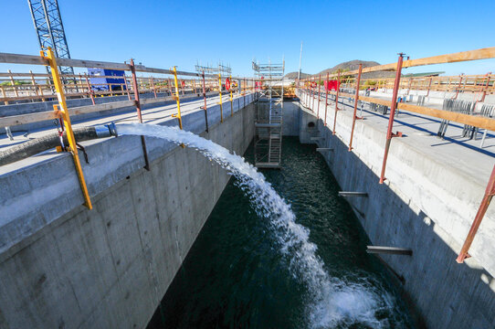 Discharge hose releasing water into a concrete treatment basin at a water reclamation facility, representing wastewater processing, flow management, and utility infrastructure