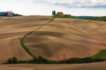 Fototapeta premium Tuscan rolling hills showing agricultural landscape and San Quirico d'Orcia, Italy.