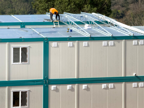 Worker on prefab container unit roof in industrial setting