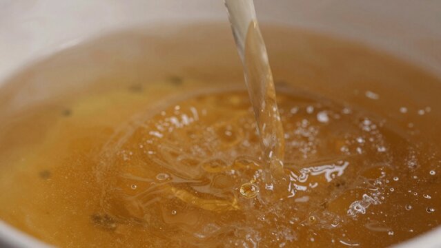 Close-up pot boiling water liquid appears warm golden-brown color small bubbles smooth texture thin white poss