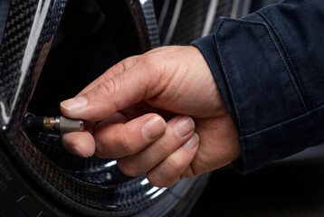 Fototapeta premium Extreme close-up of a hand adjusting a tire valve on a carbon fiber rim. The focus is on the metallic knurling and the heavy denim texture of the professional's sleeve.