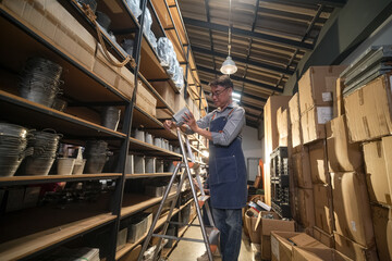 Fototapeta premium Man on ladder organizing metal buckets in a warehouse storage shelves