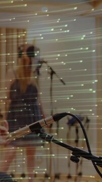 Vertical video: Guitar strumming singer tuning phones for mix at studio mic, light streaks sweeping