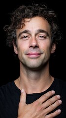 Obraz premium Confident young caucasian male smiling with hand on chest against dark background