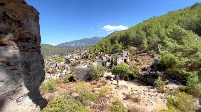 View through ruined stone window of abandoned house in Kayakoy near Fethiye, Turkey, framing ghost village buildings and pine covered hillside with distant mountains in bright summer light