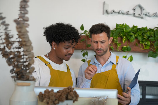 Two diverse male employees in yellow aprons discussing work at a counter