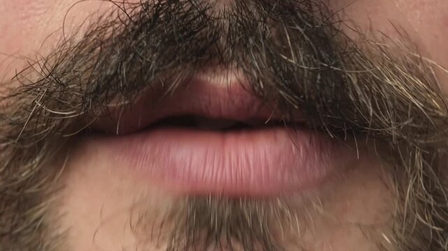 Close up shot of a young caucasian bearded and mustached man mouth speaking silently with no audio. Silent talking lip movement concept.