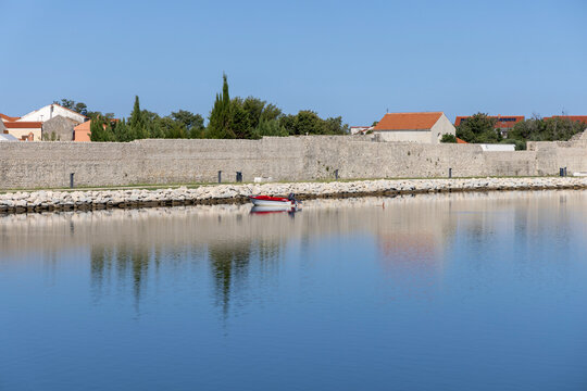 Stone defensive wall surrounding Old Town, reflection in smooth surface of Adriatic lagoon, Nin, Croatia, Dalmatia