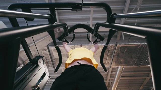 Man In The Gym Performs Assisted Pull-Ups On A Knee-Supported Machine, Viewed From Below