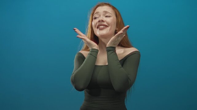 Redhead woman with exposed shoulder and open palms singing toward camera in studio; surprise expression drama performance.