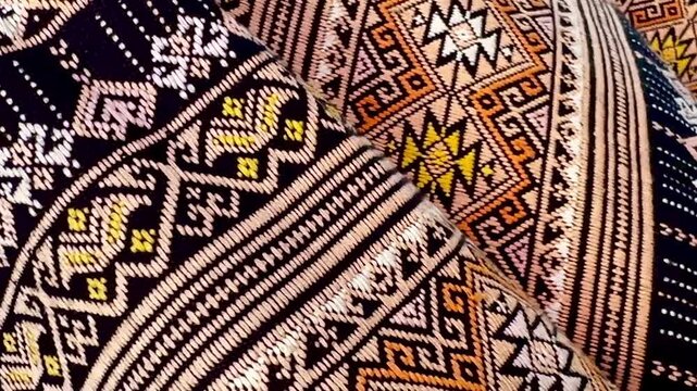 Close-up sliding shot of a traditional woven textile featuring intricate geometric patterns and earthy tones. The camera moves smoothly across the fabric, highlighting texture, craftsmanship, and c