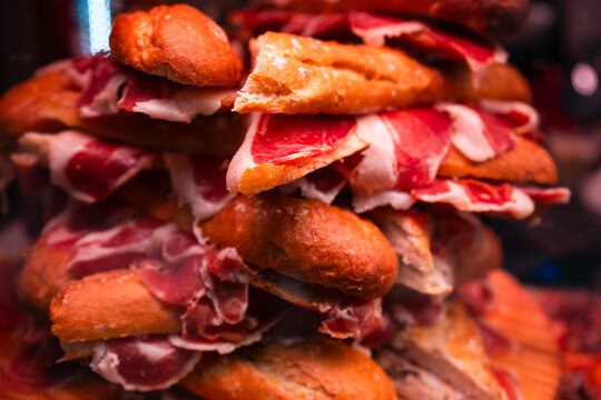 Macro-level detailed close-up of small, round brioche-like sliders filled with thinly sliced jam&oacute;n ib&eacute;rico, presented in a stacked pile.