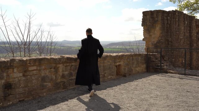 Man standing at ancient stone wall overlooking scenic valley landscape