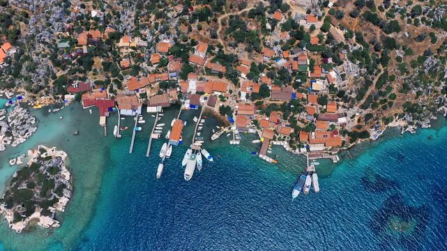 Aerial top-down view of Kalek&ouml;y village with red-roofed houses, wooden piers and tour boats moored in crystal turquoise water, Kekova, Antalya, Turkey