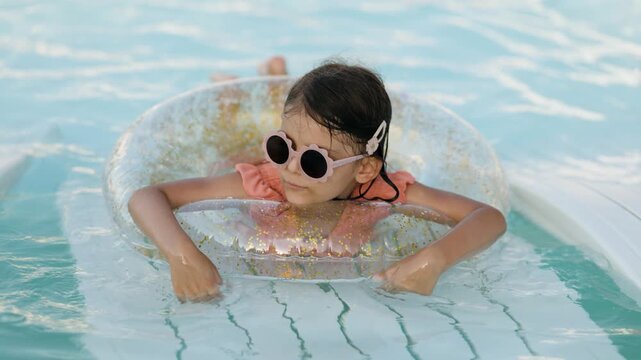 Cute funny toddler girl relaxing on inflatable toy ring floating in pool have fun during summer vacation. Child having fun in swimming pool. 