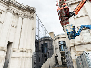 Fototapeta premium Construction lifts beside historic stone and glass civic building in London, UK under cloudy sky