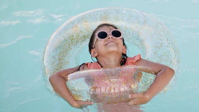 Cute funny toddler girl relaxing on inflatable toy ring floating in pool have fun during summer vacation. Child having fun in swimming pool. 