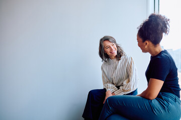 Two diverse businesswomen smiling during an informal meeting, engaging in a pleasant conversation...