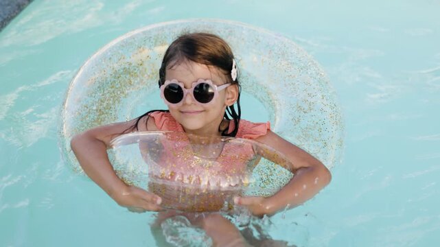 Cute funny toddler girl relaxing on inflatable toy ring floating in pool have fun during summer vacation. Child having fun in swimming pool. 