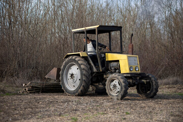 Obraz premium Farmer operating yellow tractor in rural field clearing wood