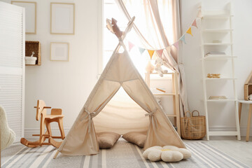 Stylish toy wigwam, furniture, pillows and decor near window in playroom. Interior design © New Africa