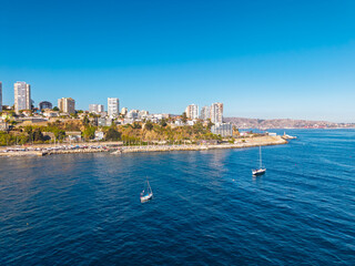 Aerial view of coastal Valparaiso city skyline with modern buildings, luxury apartments, and sailboats on the calm blue water of the Pacific Ocean in Chile