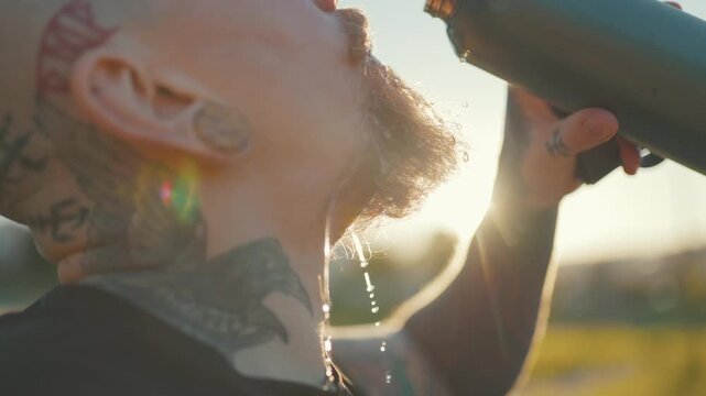 Tattooed athlete drinking water after training at sunset